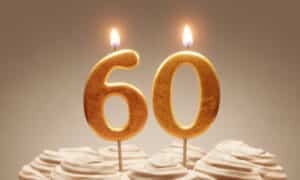 Two lit gold number candles forming 60, standing in swirls of cream buttercream icing