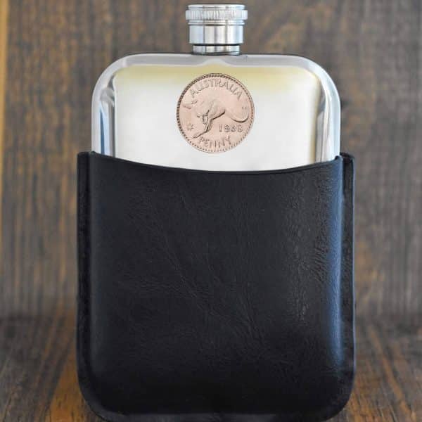 1938 Australian penny hip flask in a black leather sleeve, kangaroo coin set into the polished pewter front, dark wood backdrop