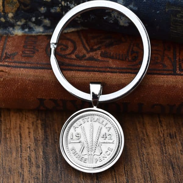 1942 Australian threepence in a polished silver bezel keyring, wheat ears design, resting on old books