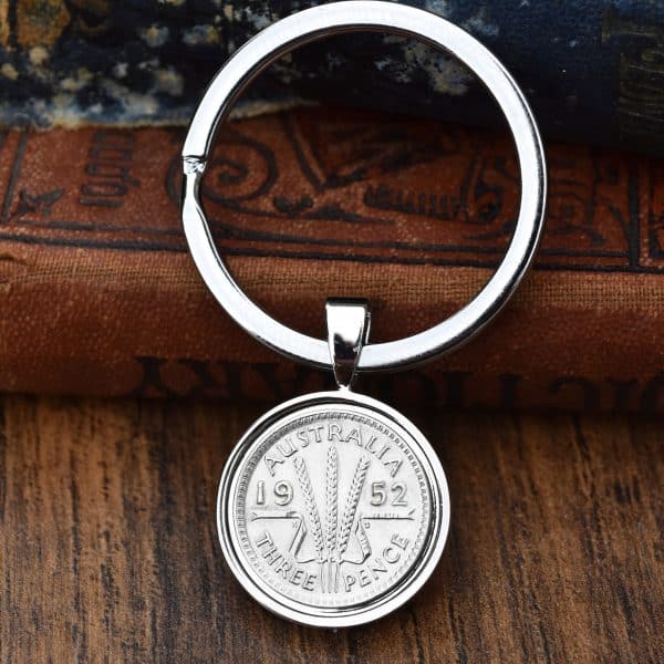 1952 Australian threepence in a polished silver bezel keyring, wheat ears design, resting on old books