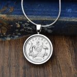 1963 Australian sixpence necklace, coin in a silver-tone bezel on a fine snake chain, dark wood and an old blue book behind