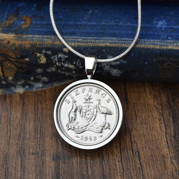 1963 Australian sixpence necklace, coin in a silver-tone bezel on a fine snake chain, dark wood and an old blue book behind