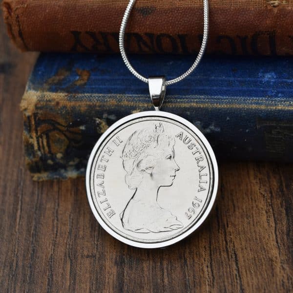 1967 Australian 20 cent coin in a silver round bezel on a snake chain, resting on an antique blue book