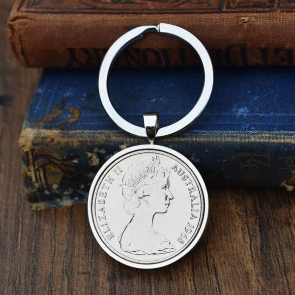 1968 Australian 20 cent coin in a silver bezel on a split-ring keyring, laid on an antique blue book