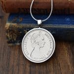 1968 Australian 20 cent coin in a silver round bezel on a snake chain, resting on an antique blue book