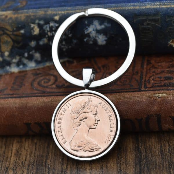 Copper 1972 Australian 2 cent coin in a silver bezel on a split-ring keyring, against antique books