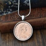 Copper 1972 Australian 2 cent coin in a silver round bezel on a snake chain, hung against antique books
