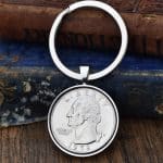 1972 United States quarter dollar in a silver-coloured bezel on a split-ring keyring, against old books