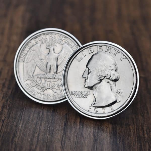 Pair of 1972 United States quarter dollars in silver-coloured bezels on dark wood, eagle and Washington sides shown