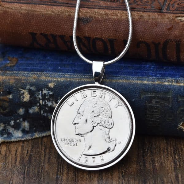 1972 United States quarter dollar set in a silver-coloured bezel on a snake chain, resting on old books