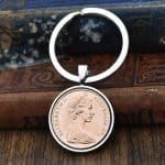 Copper 1973 Australian 2 cent coin in a silver bezel on a split-ring keyring, against antique books