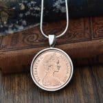 Copper 1978 Australian 2 cent coin in a silver round bezel on a snake chain, hung against antique books