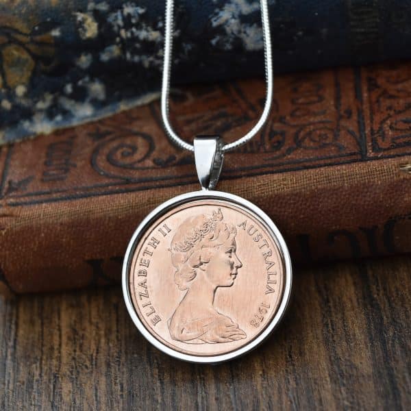 Copper 1978 Australian 2 cent coin in a silver round bezel on a snake chain, hung against antique books
