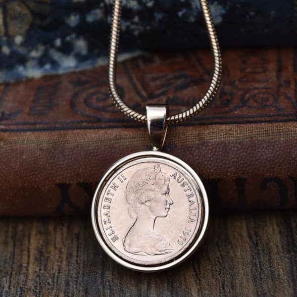 1979 Australian coin in a silver-tone bezel on a snake chain, against an old leather-bound book