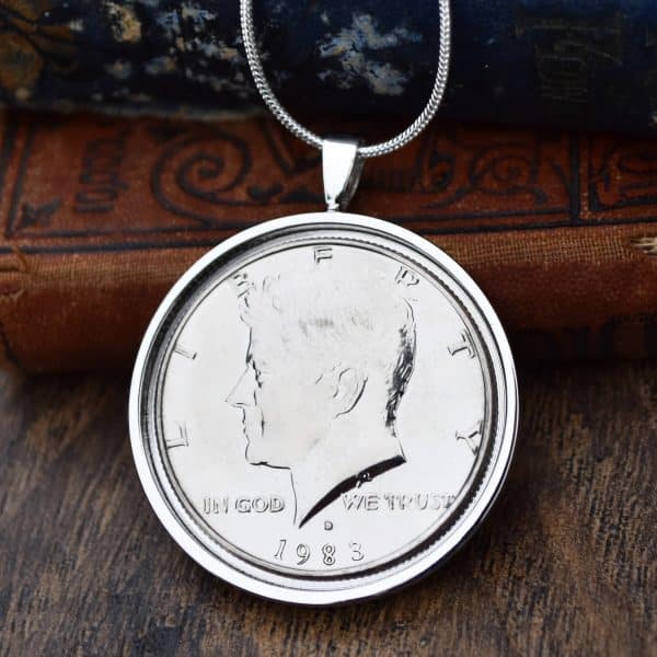 1983 American Kennedy half dollar in a silver round bezel on a snake chain, hung against antique books