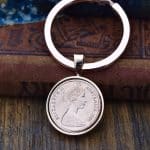 1984 Australian coin in a silver-tone bezel on a flat split-ring keyring, resting on an old leather book