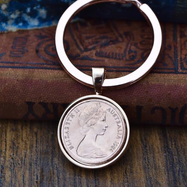 1984 Australian coin in a silver-tone bezel on a flat split-ring keyring, resting on an old leather book