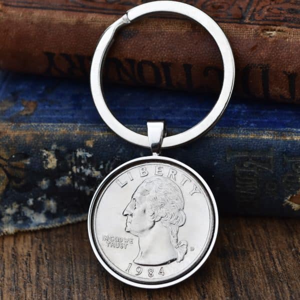 1984 United States quarter dollar in a silver-coloured bezel on a split-ring keyring, against old books