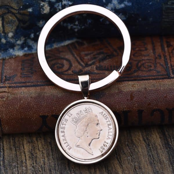 1987 Australian coin in a rose gold-tone bezel and split-ring keyring, on an old leather-bound book