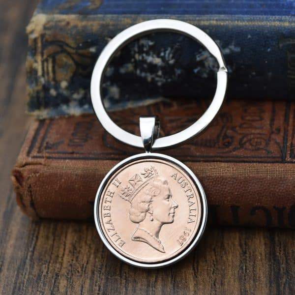 Copper 1987 Australian 2 cent coin in a silver bezel on a split-ring keyring, resting on a wooden surface