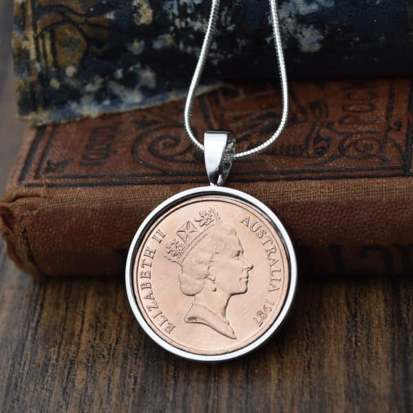 Copper 1987 Australian 2 cent coin in a silver round bezel on a snake chain, hung against antique books
