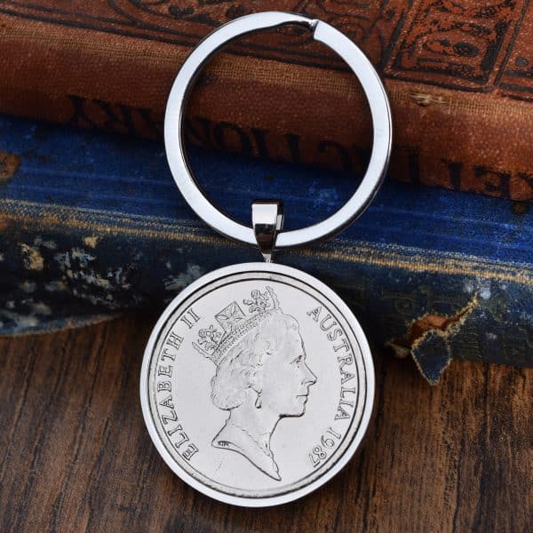 1987 Australian 20 cent coin in a silver bezel on a split-ring keyring, laid on an antique blue book