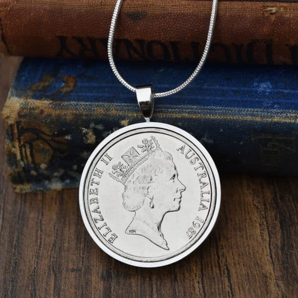 1987 Australian 20 cent coin in a silver round bezel on a snake chain, resting on an antique blue book