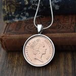 Copper 1988 Australian 2 cent coin in a silver round bezel on a snake chain, hung against antique books