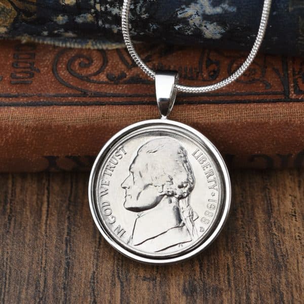1988 American Jefferson nickel in a polished silver bezel pendant on a snake chain, against an old leather book