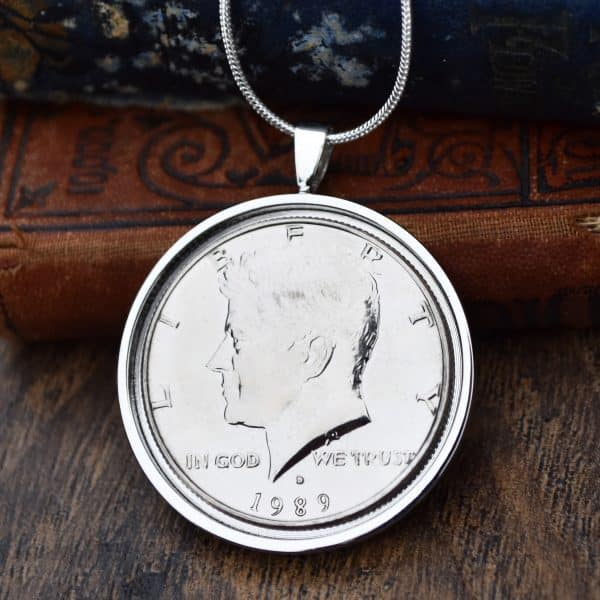 1989 American Kennedy half dollar in a silver round bezel on a snake chain, hung against antique books