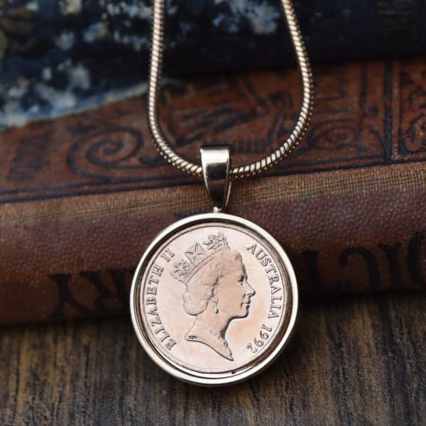 1992 Australian coin in a silver-tone bezel on a snake chain, against an old leather-bound book