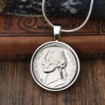 1993 American Jefferson nickel in a polished silver bezel pendant on a snake chain, against an old leather book