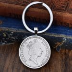 1994 Australian 20 cent coin in a silver bezel on a split-ring keyring, laid on an antique blue book