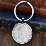 1997 Australian 20 cent coin in a silver bezel on a split-ring keyring, laid on an antique blue book