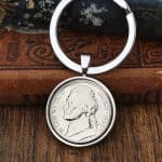 1998 American Jefferson nickel set in a polished silver bezel keyring, leaning on a leather-bound book