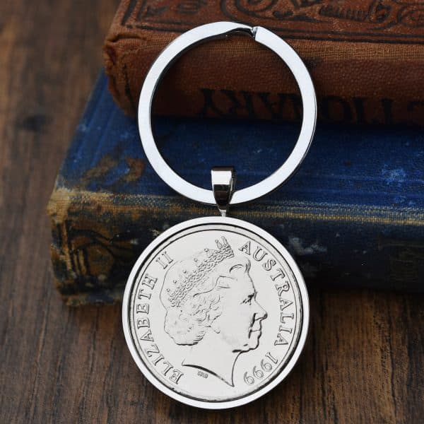 Australian coin dated 1999 in a silver-tone bezel on a split-ring keyring, Elizabeth II obverse, against old books