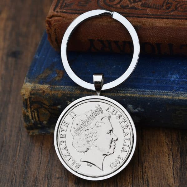 Australian coin dated 2001 in a silver-tone bezel on a split-ring keyring, Elizabeth II obverse, against old books