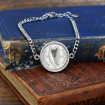 1935 Saorstat Eireann harp coin in a silver-tone bezel on a curb chain bracelet, resting on old blue and red books