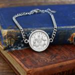 1939 Australian sixpence in a silver-tone bezel on a curb-chain bracelet, coat of arms reverse, resting on old blue and red books