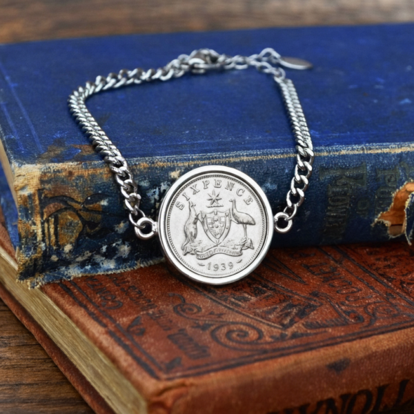 1939 Australian sixpence in a silver-tone bezel on a curb-chain bracelet, coat of arms reverse, resting on old blue and red books