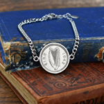 1942 Irish sixpence in a silver-tone round bezel on a curb chain bracelet, laid on a faded blue book cover