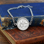 1945 Australian sixpence in a silver-tone bezel on a curb-chain bracelet, coat of arms reverse, resting on old blue and red books