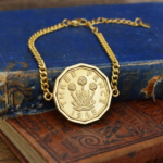 1945 threepence in a gold-coloured bracelet, thrift plant design, resting on old blue and red books