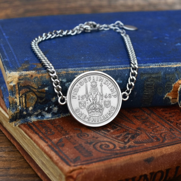 1948 one shilling set into a silver-coloured bracelet with curb chain, Scottish lion and crown reverse, on a worn blue book and a red book