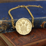 1948 threepence in a gold-coloured bracelet, thrift plant design, resting on old blue and red books