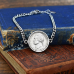 Silver-coloured chain bracelet holding a 1949 US nickel in a plain bezel, on two old hardback books