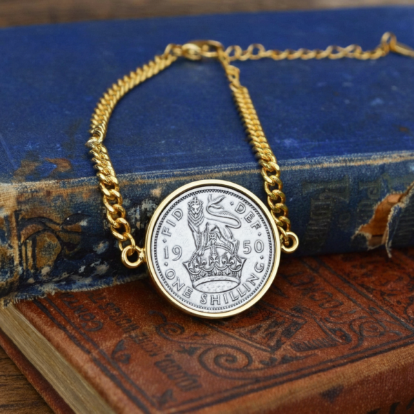 1950 one shilling coin in a gold-coloured bezel on a gold curb chain bracelet, laid on worn antique books