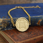 1954 threepence in a gold-coloured bracelet, crowned portcullis design, on old blue and red books
