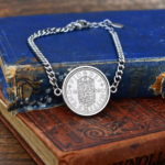 1955 one shilling coin in a silver-coloured bezel on a curb chain bracelet, English shield reverse, resting on old cloth-bound books