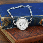 Curb chain bracelet with a 1955 US nickel set in a silver-coloured bezel, on an old blue and tan book